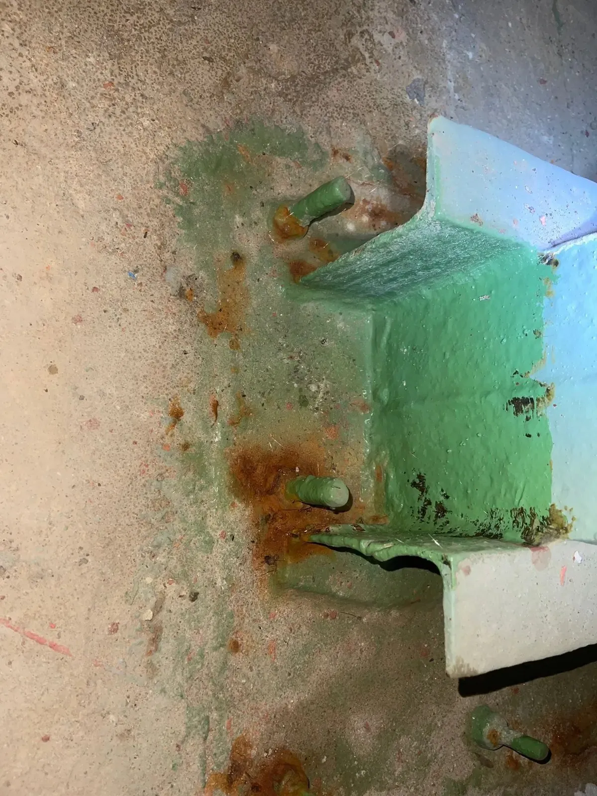 Placa de anclaje con óxido en pernos y bordes saliendo bajo la pintura