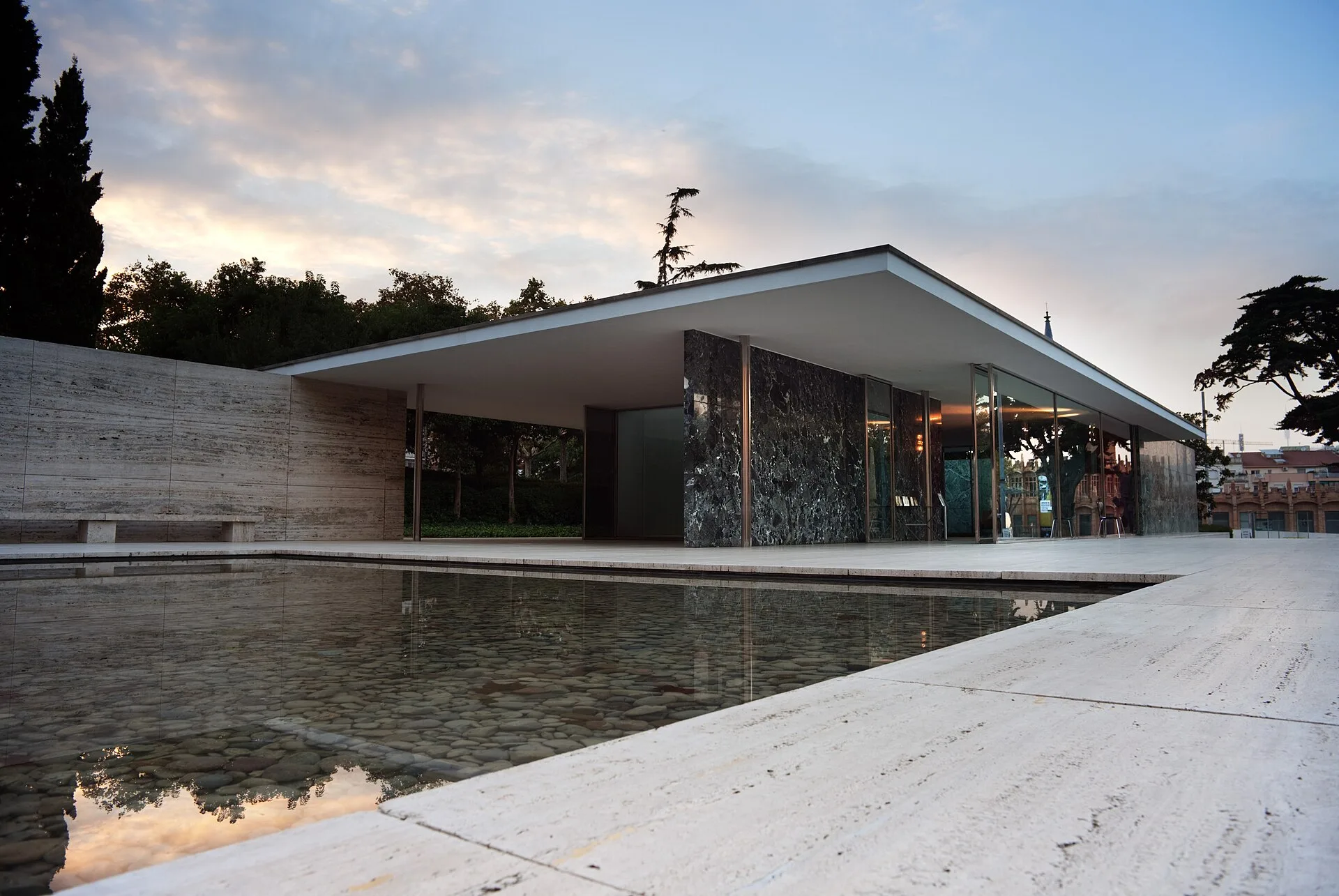 Pabellón de Alemania de Mies van der Rohe en Barcelona, con su estanque reflejando la cubierta y los muros de piedra al atardecer