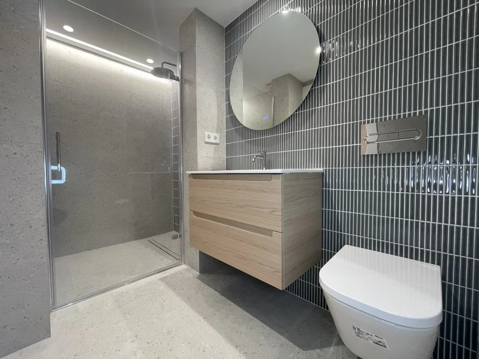 Baño terminado: plato de ducha, alicatado vertical y mueble suspendido