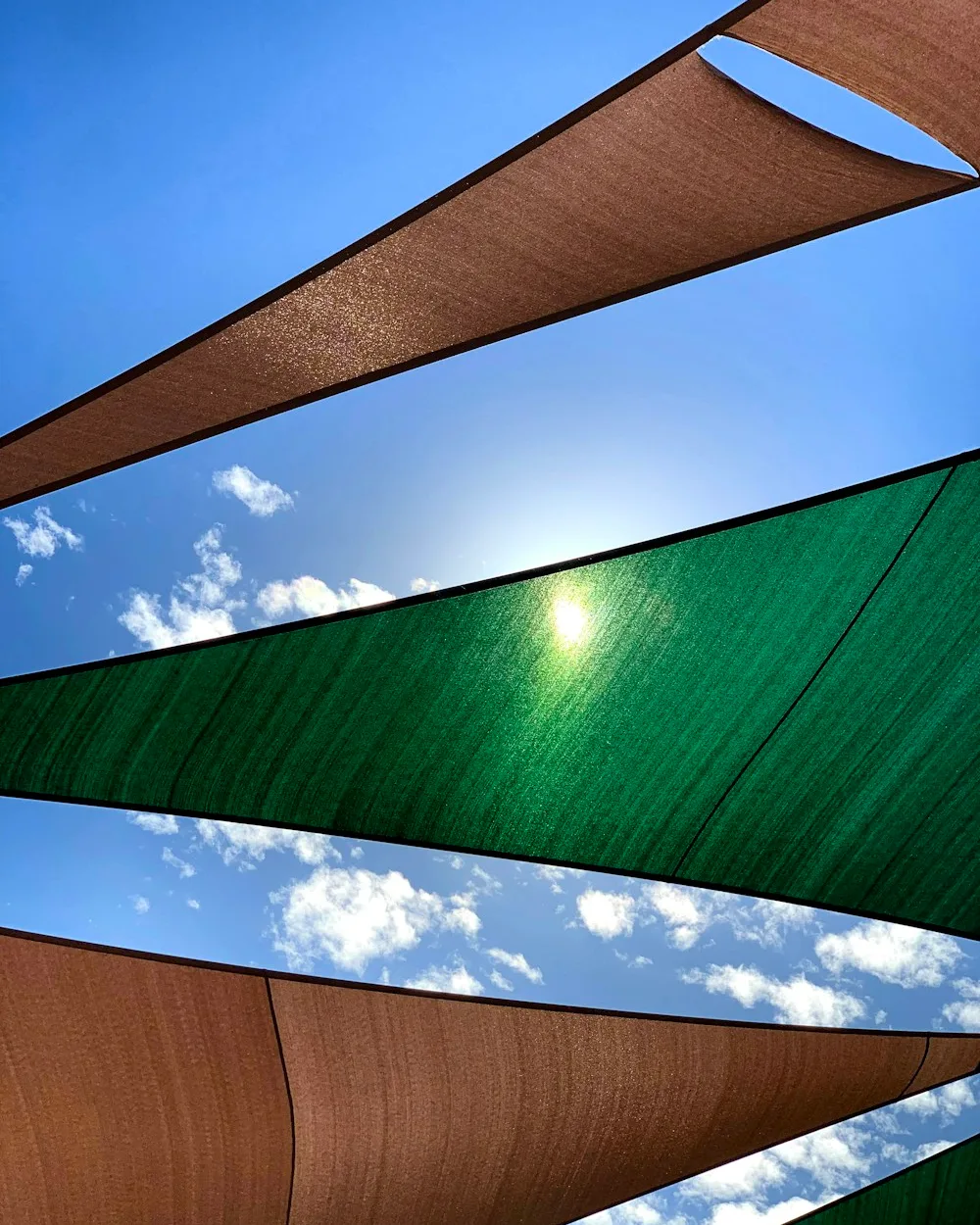 Velas de sombra marrones y verdes vistas desde abajo con el sol detrás